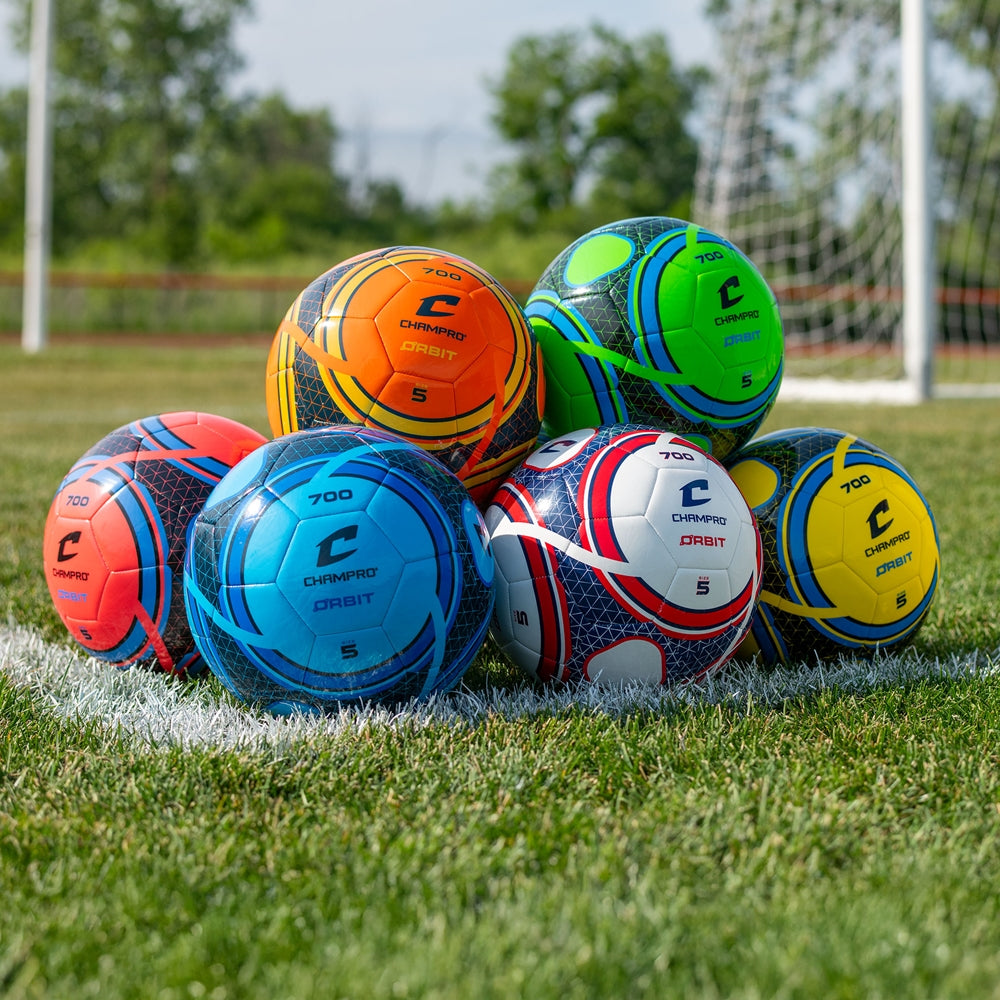 Bright Champro Orbit soccer balls stacked on a grass field with a goal in the background