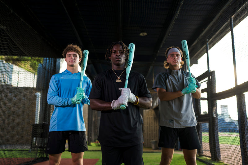 Three individuals holding baseball bats in a batting cage.