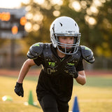 Young football player in a white Schutt helmet and protective gear sprinting on a field.