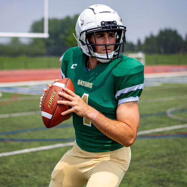 Football player in a green Champro Force jersey wearing a helmet and holding a football on a field