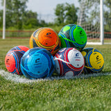 Bright Champro Orbit soccer balls stacked on a grass field with a goal in the background